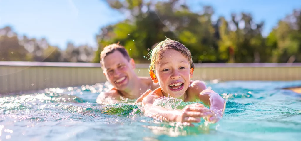 Vater und Sohn beim Schwimmen im Strömungskanal, während die Sonne auf den Wellen reflektiert.