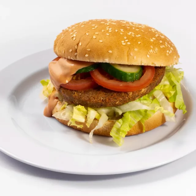 Ein Falafel Burger mit Salat, Gurke, Tomate und hausgemachter Burgersauce im Sesambrötchen vor einem weißen Hintergrund