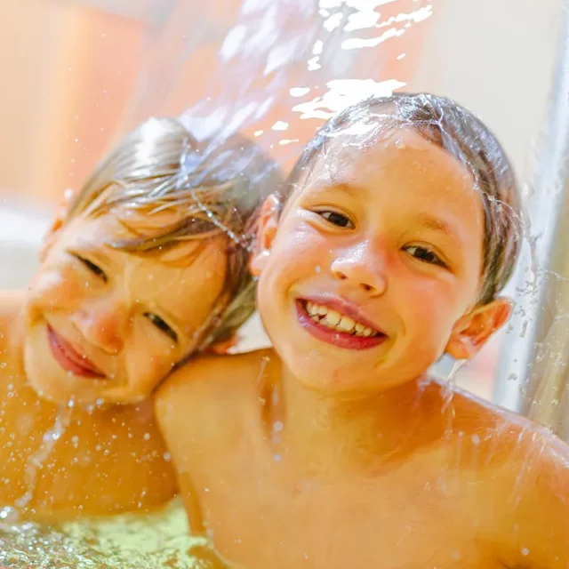 Zwei Jungs unter einem unserer Wasserpilze im Kinderbereich. Das Wasser umgibt ihre lächelnden Gesichter.