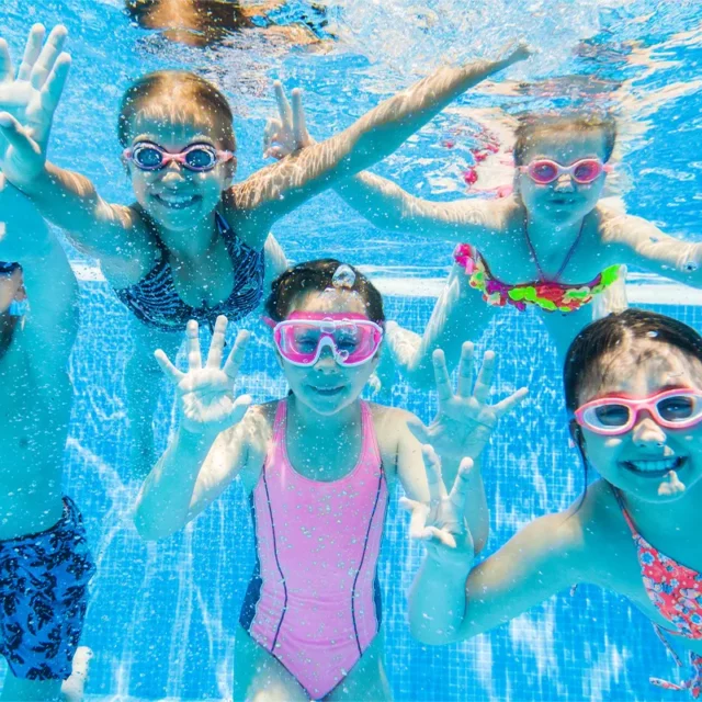 Fünf Kinder, die unter Wasser mit bunten Schwimmbrillen in die Kamera lächeln.