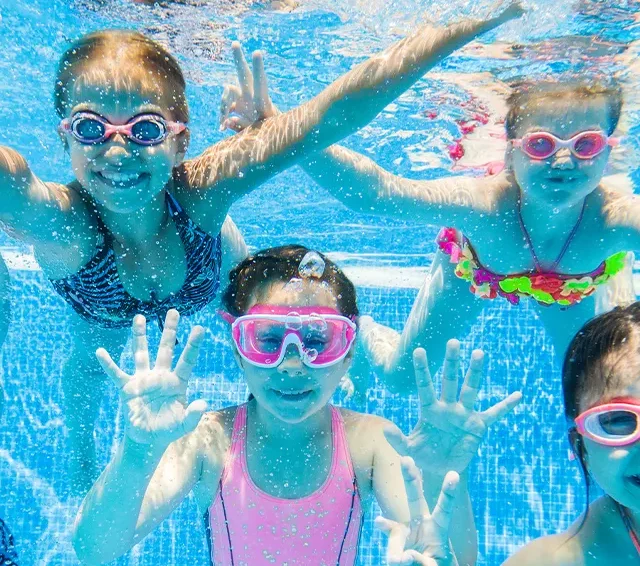 Fünf Kinder, die unter Wasser mit bunten Schwimmbrillen in die Kamera lächeln.