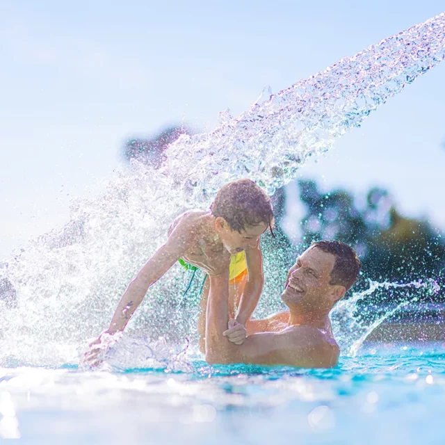 Vater und Sohn spielen, umgeben von Wasserspritzern, unter den Schwallduschen im Strömungskanal.